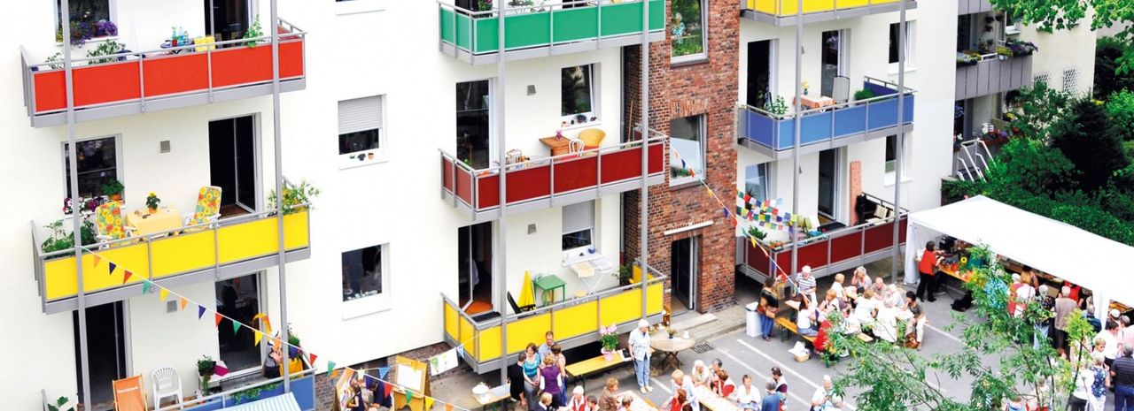 ein Wohnkomplex mit bunten Balkonen, überall sind Menschen, die gemeinsam sitzen 